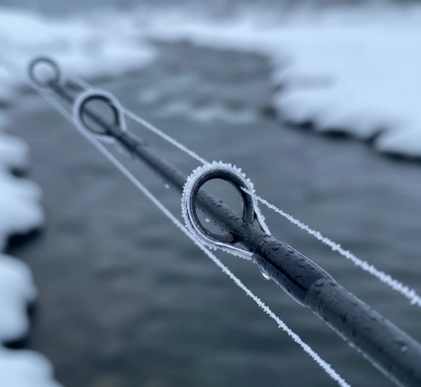 Close-up of spinning rod guides with frost, winter pike fishing conditions, cold water background.