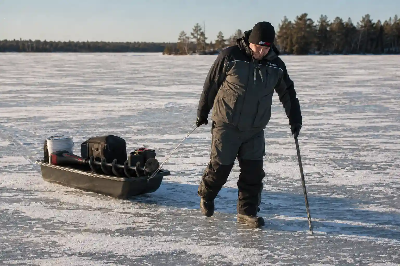 MFG tester checking ice conditions in a floating ice fishing suit while pulling a loaded gear sled