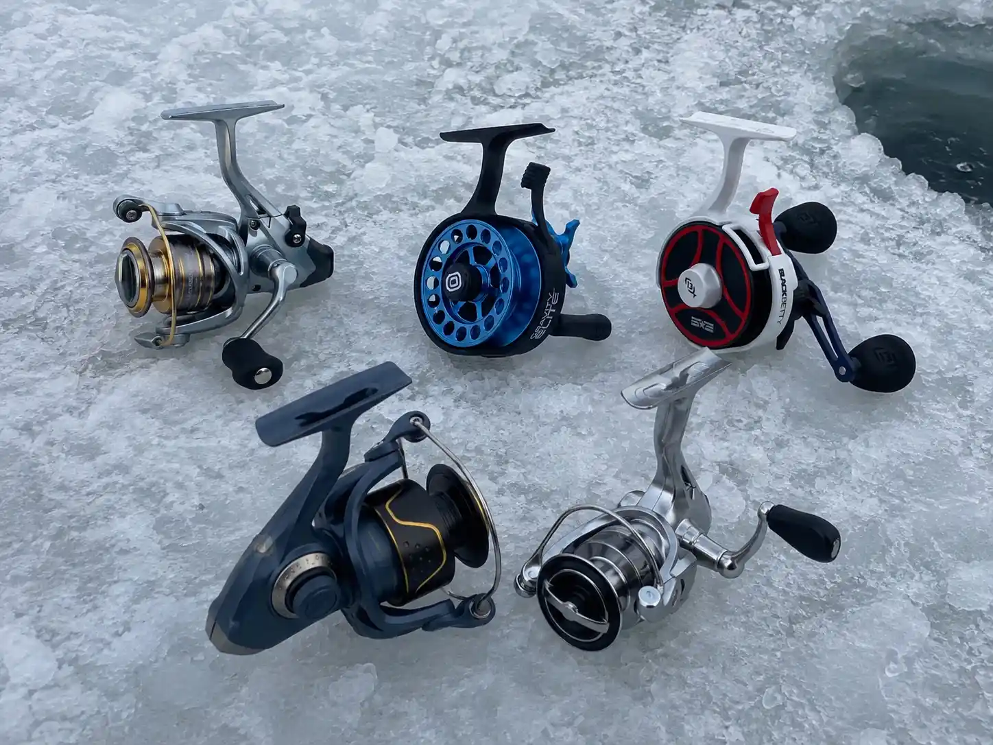 Five ice fishing reels we field-tested for pike, laid out on the ice next to our fishing hole