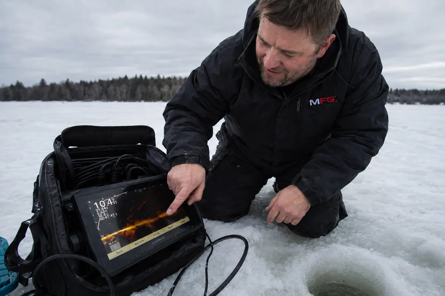 MFG angler checking a Garmin ice fishing fish finder screen next to a hole in the ice