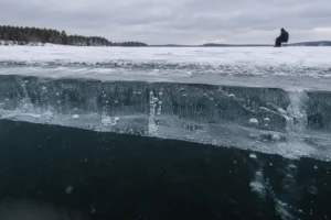 Ice fishing safety on thick clear ice with an MFG angler fishing in the distance