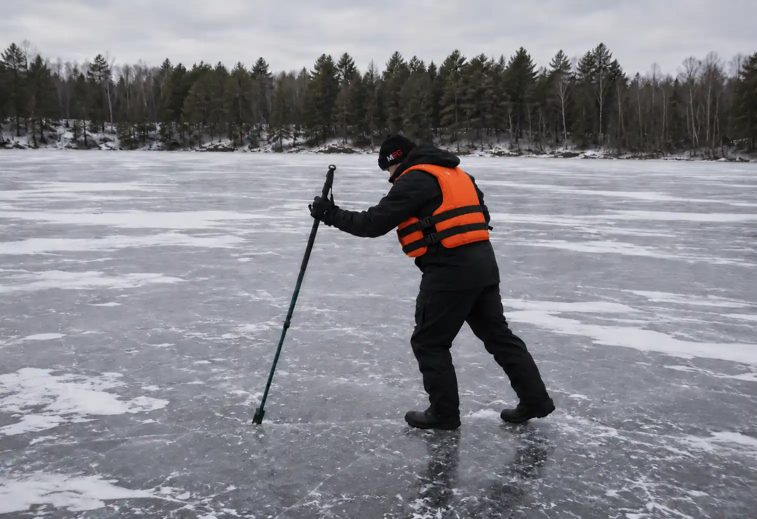 Checking ice thickness with a spud bar and wearing a life jacket before ice fishing for pike